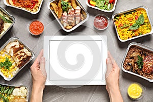 Top view of woman holding tablet over grey table with lunchboxes. Healthy food delivery