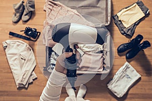 Top view on the woman holds hair dryer packing clothes in the open suitcase. Travel
