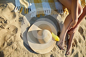 Top view Woman leg sitting on the sandy beach, near hat and sunscreen