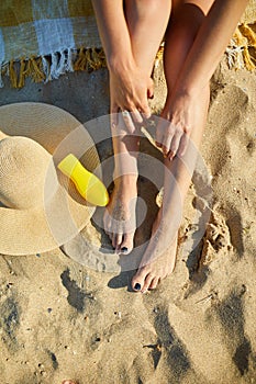 Top view Woman leg sitting on the sandy beach, near hat and sunscreen