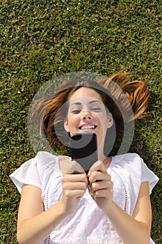 Top view of a woman lying on the grass texting on a smart phone