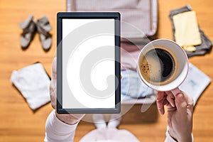 Top view of woman packing a luggage for a new journey. Female standing above suitcase with electronic note pad and cup of coffee.