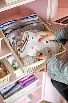 Top view woman putting case box neatly folded clothes on shelf in pink feminine cupboard cleanup