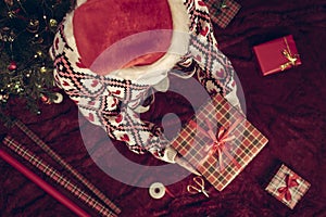 Top view of woman in red santa claus hat holding wrapping christmas gifts boxe for family standing on fluffy plaid near christmas.