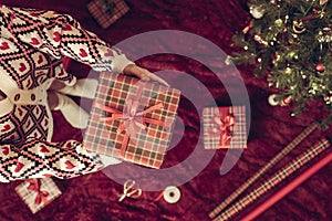 Top view of woman in red santa claus hat holding wrapping christmas gifts boxe for family standing on fluffy plaid near christmas.