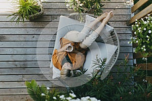 Top view of woman relaxing in the garden, drinking coffee and lying on patio chair. Mother having moment to herself