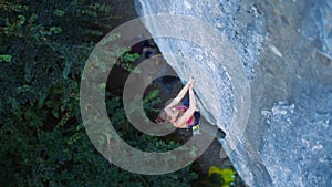 Top view woman rockclimber climbing on tough sport route, rock climber resting and chalking hands hanging on the cliff.