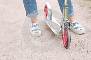 Top view on woman's feet in sneakers on the scooter. Girl riding scooter in the park. Outdoor activities. lifestyle