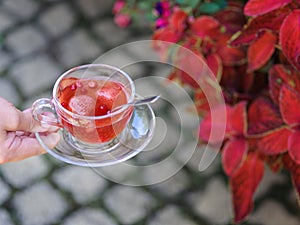 A top view of a girl`s hand with a cup of fruity tea on a natural background. Strawberry balsamico herbal tea.