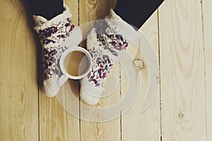 Top view of woman`s legs in warm socks with a cup of coffee with milk