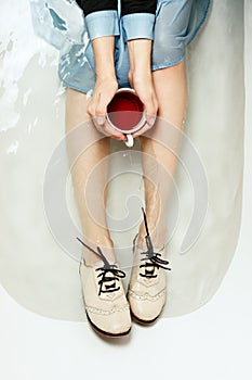 Top view of woman`s sitting in a bathtub with a cup of red tea