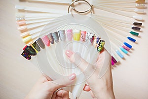 Top view woman selects yellow color shellac nail polish.Nail technician shows the color palette of nail services in