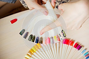 Top view woman selects yellow color shellac nail polish.Nail technician shows the color palette of nail services in beauty salon.