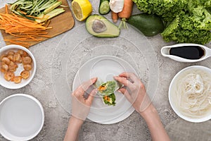 Top view of woman serving tasty spring rolls on white plate.