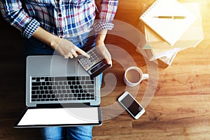 Top view of woman shopping online via laptop computer ,using calculator for calculate value price on wooden floor