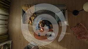 Top view of a woman sitting on a living room couch in front of a coffee table with a bottle of alcohol. The woman is