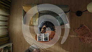 Top view of a woman sitting on a living room couch in front of a coffee table with a bottle of alcohol and a glass