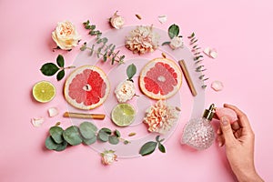 Top view of woman spraying perfume on pink background, flowers and citrus fruits representing aroma