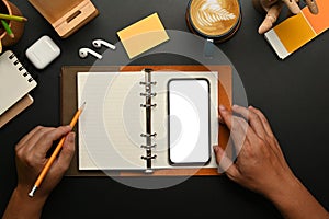 Top view of woman using mobile phone and making notes on blank notepad