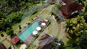 Top view of woman walking along infinity swimming pool in jungle highlands. Luxury villa in Bali aerial.