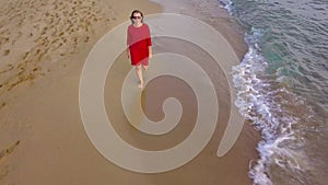 Top view of a woman walking barefoot along wet sand beach. Running wave is washing away footprints on the sand