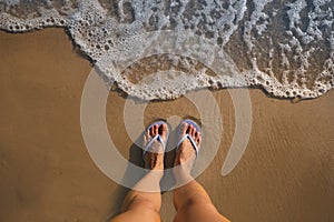 Top view of woman wearing beach slippers on sandy seashore, closeup