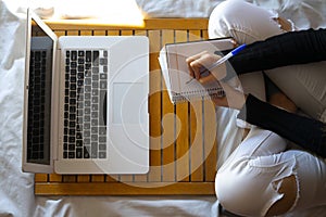 Top view of a woman working in bed and writing on her datebook