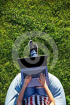 Top view. Woman working on laptop pc computer with blank black empty screen to copy space in park on green grass