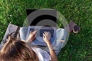 Top view. Woman working on laptop pc computer with blank black empty screen to copy space in park on green grass