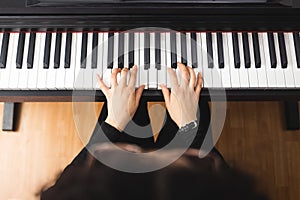 Top view of woman's hands playing piano by reading sheet music.