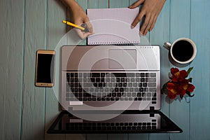 Top view of womans hand write something on blank paper near laptop and telephone