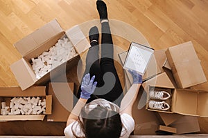 Top view of women in mask and gloves working at home on tablet on wooden floor with parcel. Selling, buying online on