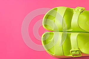 Top view of women's trendy pool sandals in green neon color isolated on the pink summer background.