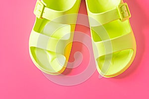 Top view of women's trendy pool sandals in green neon color isolated on the pink summer background.