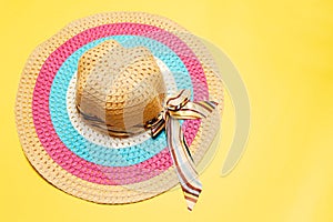 Top view of women summer hat with ribbon bow and lines of white, pink and blue colors on yellow background.