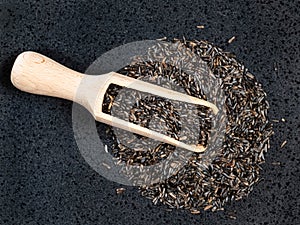 Top view of wood scoop on niger seeds on black photo