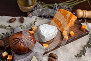 Top view of a wooden board with Neuchatel and Colby orange cheese served with bread and herbs