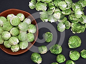 top view of a wooden bowl of cleaned and uncleaned fresh raw Brussels sprouts on a black slate plate