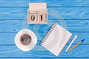 top view of wooden calendar with date of 1st may, coffee cup, blank textbook and pens, international workers day concept