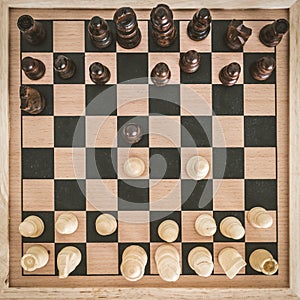 Top view on wooden chess board with chess figures ready for the game and man's hand making chess move on white wooden table