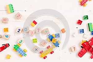 Top view on wooden cubes with numbers and colorful toy bricks on a white wooden background. Toys in the table