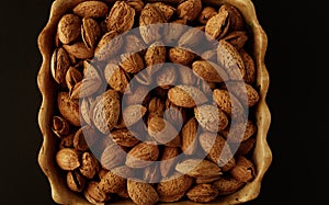 Top view of wooden cup bowls with a handful of pecans, almonds on a black background.