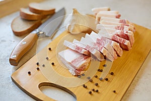 Top view of wooden cutting board with salo, peppercorn, slices of bread, garlic and knife, lunch time, traditional Ukrainian food