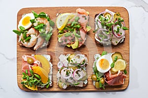 Top view of wooden cutting board with tasty smorrebrod sandwiches on white marble surface. photo