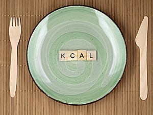 Top view of wooden letter blocks with kcal word on green plate with wooden knife and fork