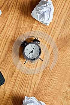 Top view of wooden office desk with clock, crumpled paper balls