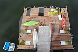 Top view of wooden pier with launchers - kayaks and paddles and life vests scattered around and a paddleboat in the water photo