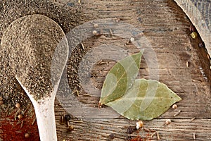 Top view of a wooden spoon full of black pepper and bay leaf on wooden barrel background, selective focus.