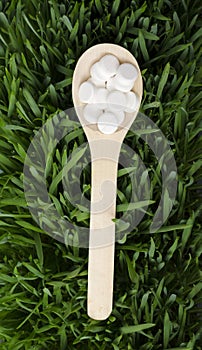 Top view of wooden spoon full of white pills on the green grass.Concept of organic and natural medical treatments