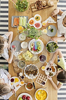 Top view of a wooden table with variety of fresh organic vegetables, fruit, salad and herbs. Kids eating delicious products